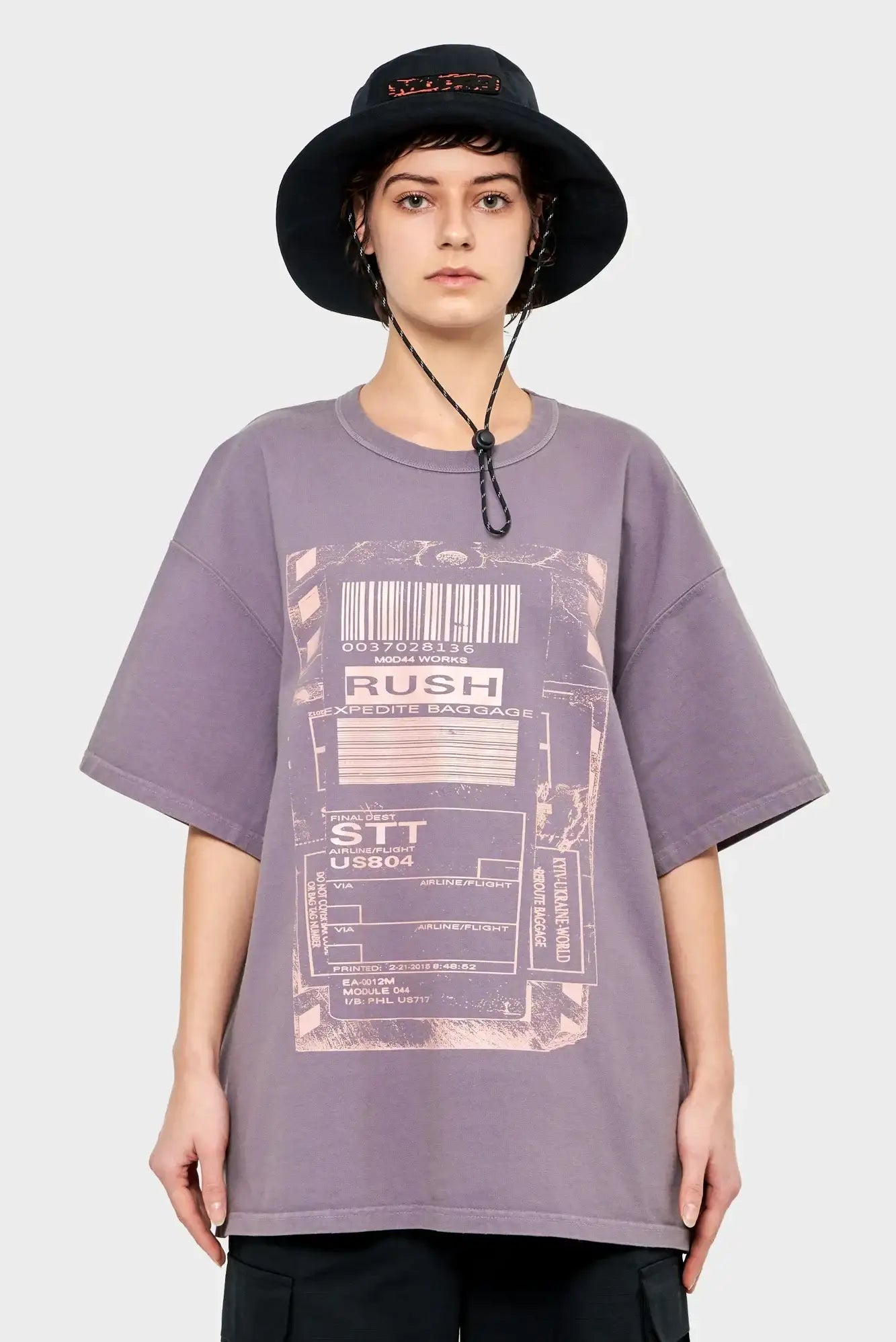 Osoba w fioletowym t-shircie z graficznym nadrukiem bagażowym i czarnym bucket hat, moda streetwear