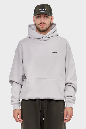 Mężczyzna w jasnej, oversize'owej bluzie z kapturem bareen i czapce z daszkiem SILENCE, styl streetwear.