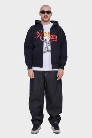 Mężczyzna w czarnej rozpinanej bluzie z kapturem i napisem, białej koszulce z grafiką, szerokich jeansach, sneakersach i okularach przeciwsłonecznych, styl streetwear
