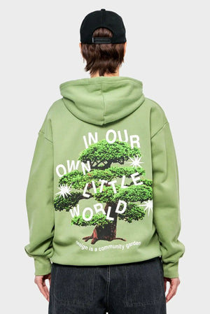 Zielona bluza z kapturem, nadruk drzewo bonsai i napis IN OUR OWN LITTLE WORLD, moda streetwear.