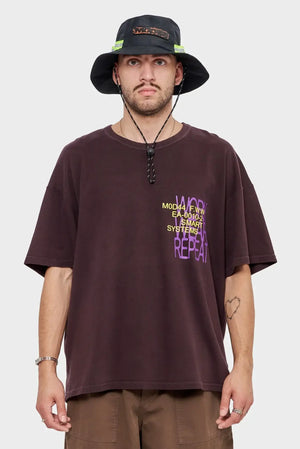 Mężczyzna w brązowej koszulce z nadrukiem MOD44, bucket hat, styl streetwear.