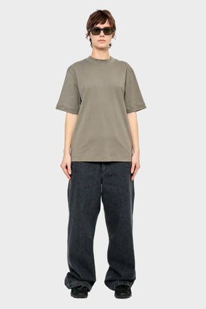 Osoba w luźnym szarym t-shircie, szerokich czarnych jeansach i okularach przeciwsłonecznych, styl streetwear.