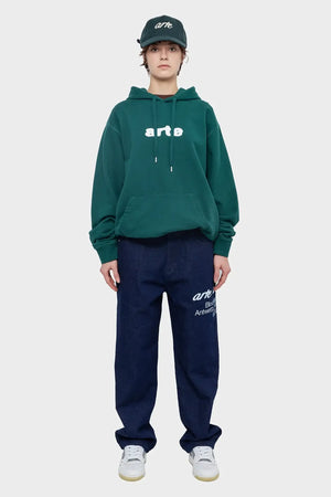 Modelka w zielonej bluzie z kapturem, czapce z daszkiem i granatowych jeansach z nadrukiem, styl streetwear