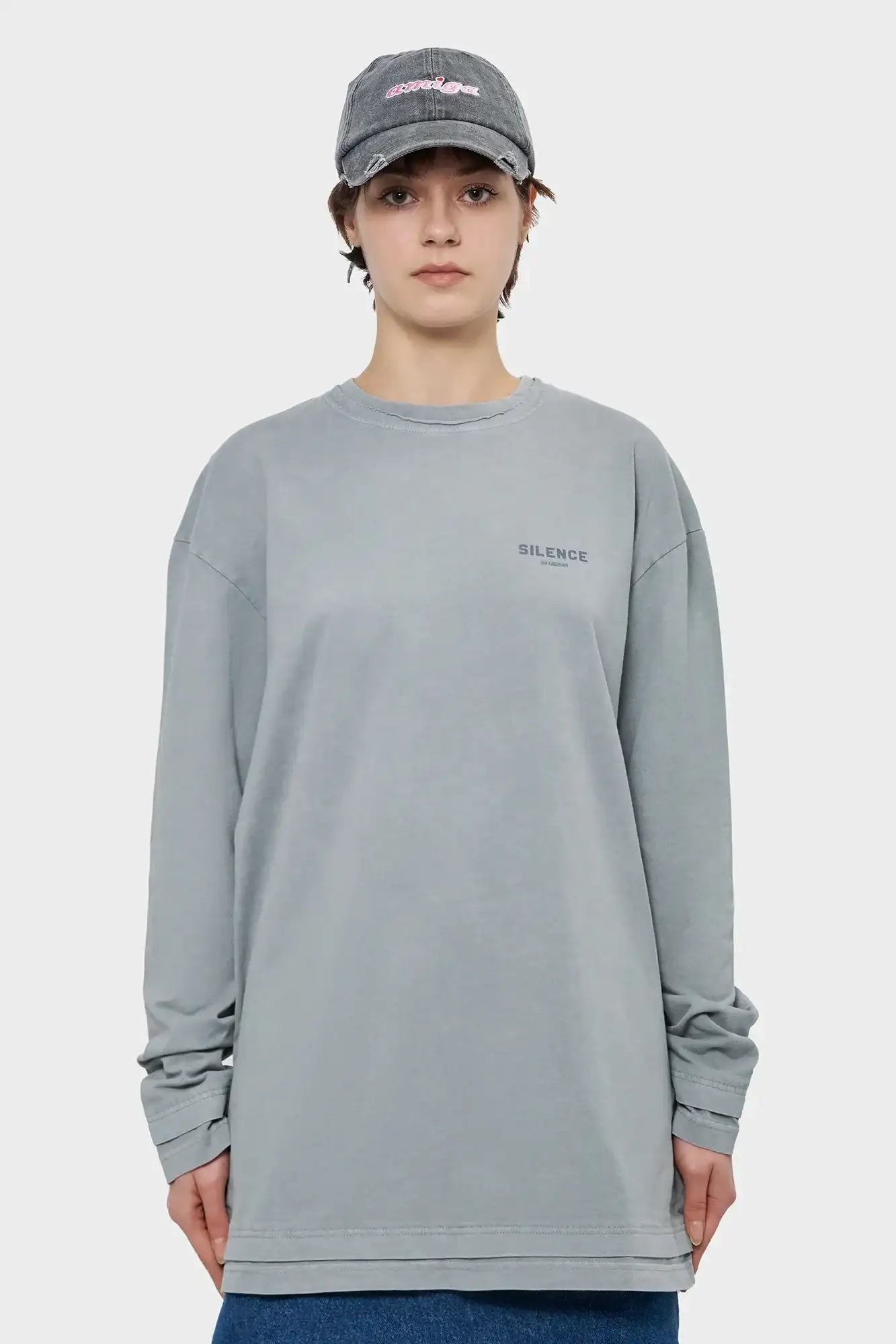 Osoba w szarej bluzie z napisem 'SILENCE' i czapce z daszkiem na jasnym tle, moda streetwear.