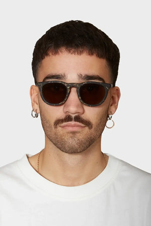 Mężczyzna w okularach przeciwsłonecznych z ciemnymi szkłami, białej koszulce i kolczykami, modny styl streetwear