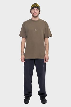 Mężczyzna w brązowym t-shircie, ciemnych spodniach i czapce z żółtym wzorem, styl streetwear