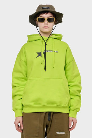 Modelka w limonkowej bluzie z nadrukiem gwiazdy, oliwkowym kapeluszu RIOTDIVISION i okularach, streetwear