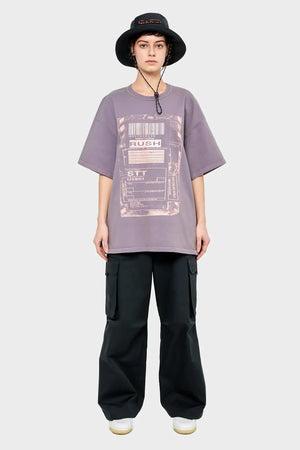 Osoba w luźnym fioletowym t-shircie z nadrukiem, czarnych bojówkach i czarnym kapeluszu typu bucket hat