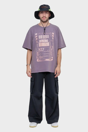 Mężczyzna w fioletowym t-shircie z nadrukiem, czarnych bojówkach i bucket hat, styl streetwear