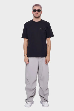 Mężczyzna w czarnym t-shircie z napisem, szarych szerokich spodniach i białych sneakersach