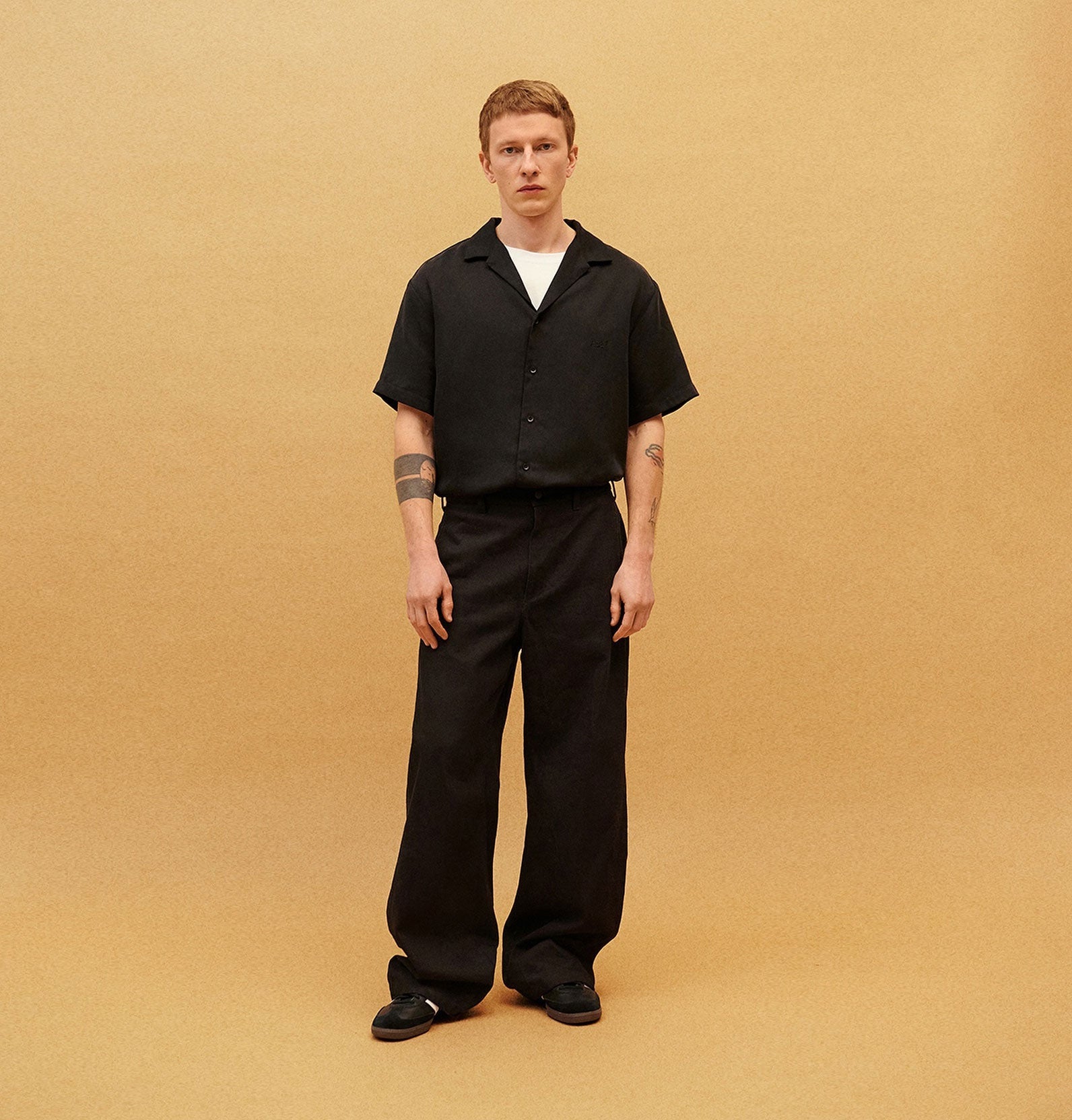 Mężczyzna w czarnym zestawie oversize, krótki rękaw, szerokie spodnie, minimalistyczne tło