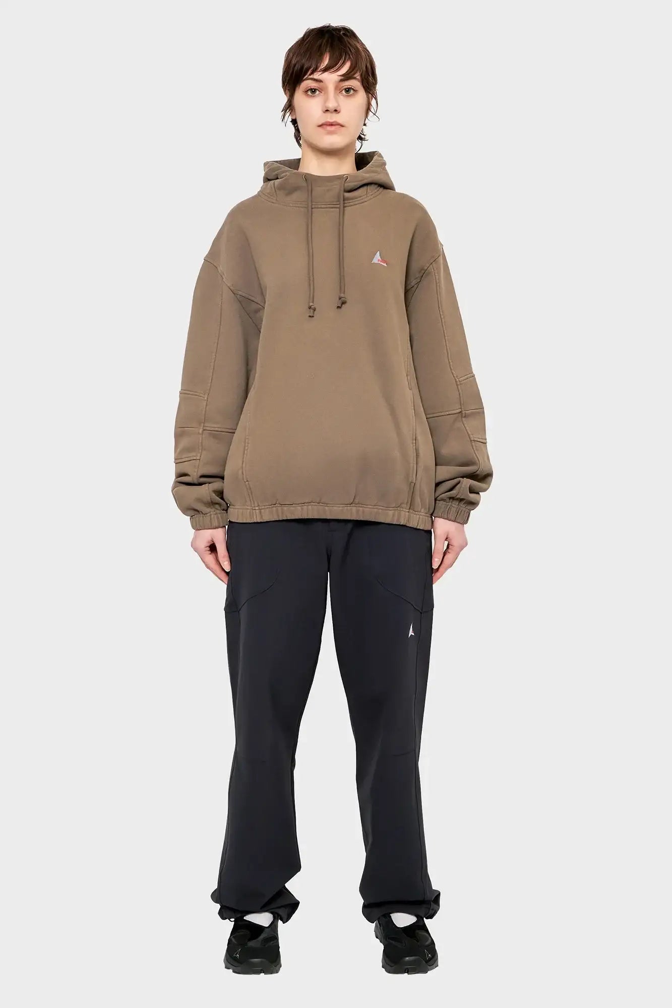 Osoba w beżowej bluzie z kapturem i czarnych spodniach, minimalistyczna stylizacja streetwear