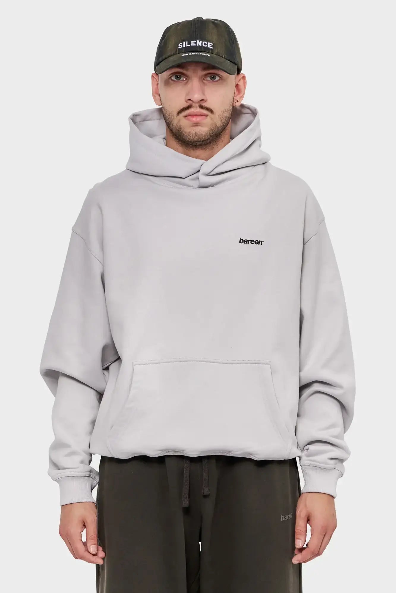 Mężczyzna w jasnej, oversize'owej bluzie z kapturem bareen i czapce z daszkiem SILENCE, styl streetwear.