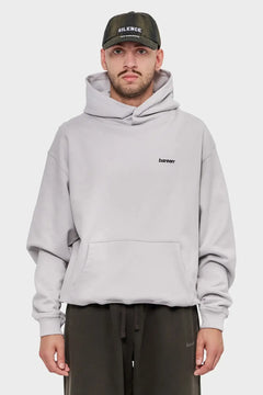Mężczyzna w jasnej, oversize'owej bluzie z kapturem bareen i czapce z daszkiem SILENCE, styl streetwear.
