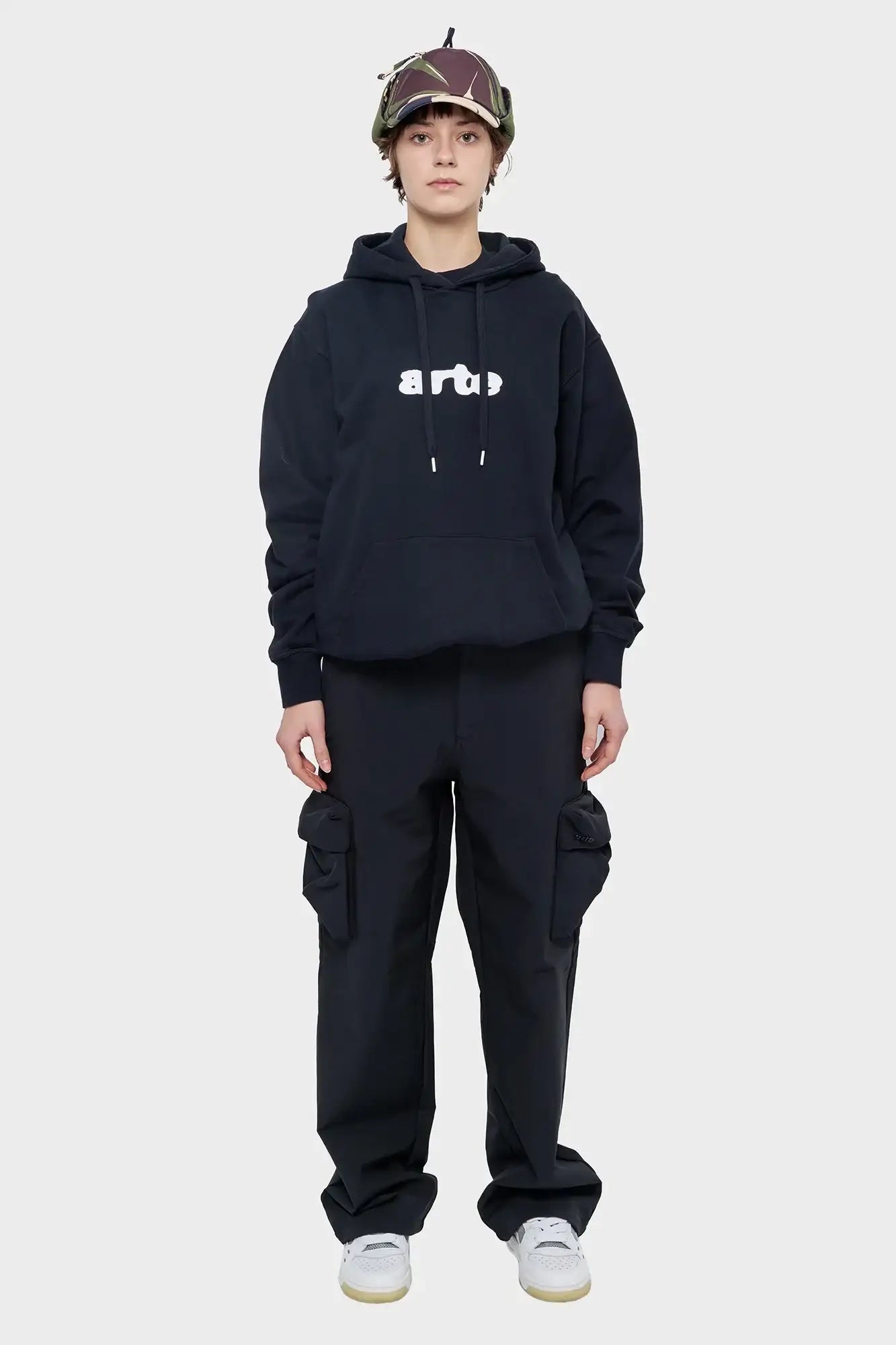 Modelka w czarnej bluzie Arte, bojówki cargo, buty sportowe, czapka z daszkiem, streetwear
