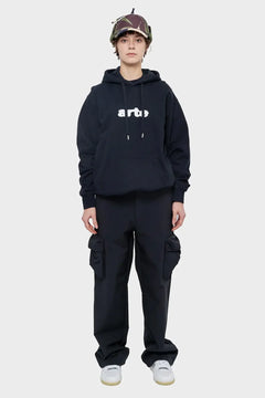 Modelka w czarnej bluzie Arte, bojówki cargo, buty sportowe, czapka z daszkiem, streetwear