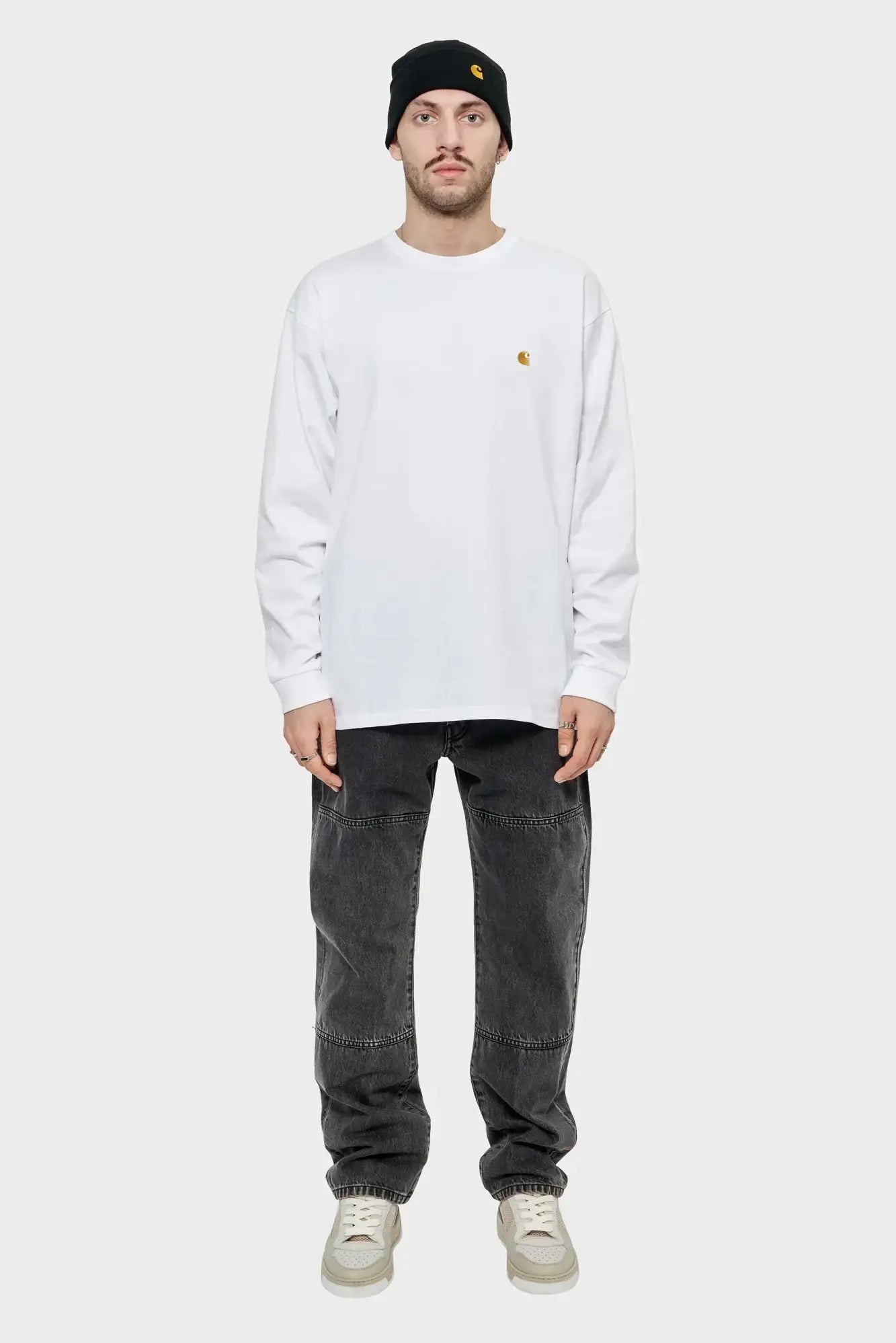 Mężczyzna w białej bluzie long sleeve, czarnej czapce i czarnych jeansach, minimalistyczny styl uliczny.