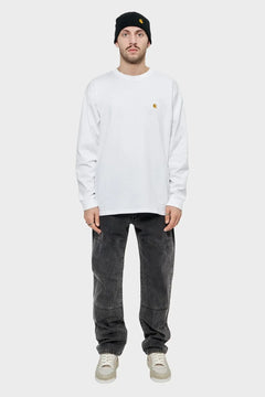 Mężczyzna w białej bluzie long sleeve, czarnej czapce i czarnych jeansach, minimalistyczny styl uliczny.
