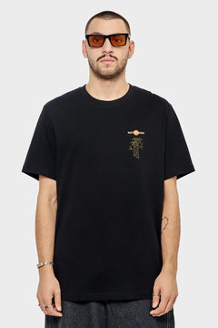 Mężczyzna w czarnej koszulce RIOTDIVISION, pomarańczowe okulary przeciwsłoneczne, styl streetwear