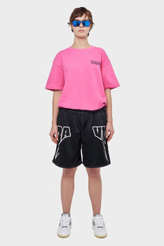 Osoba w różowej koszulce, czarnych sportowych szortach i białych sneakersach, modne okulary lustrzane, styl streetwear