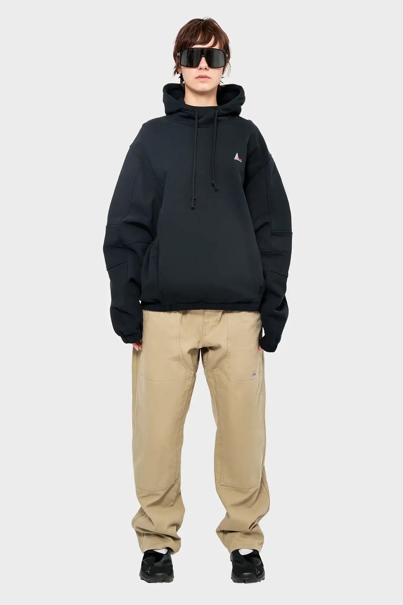Osoba w czarnej bluzie z kapturem, beżowych spodniach i dużych okularach przeciwsłonecznych, styl streetwear