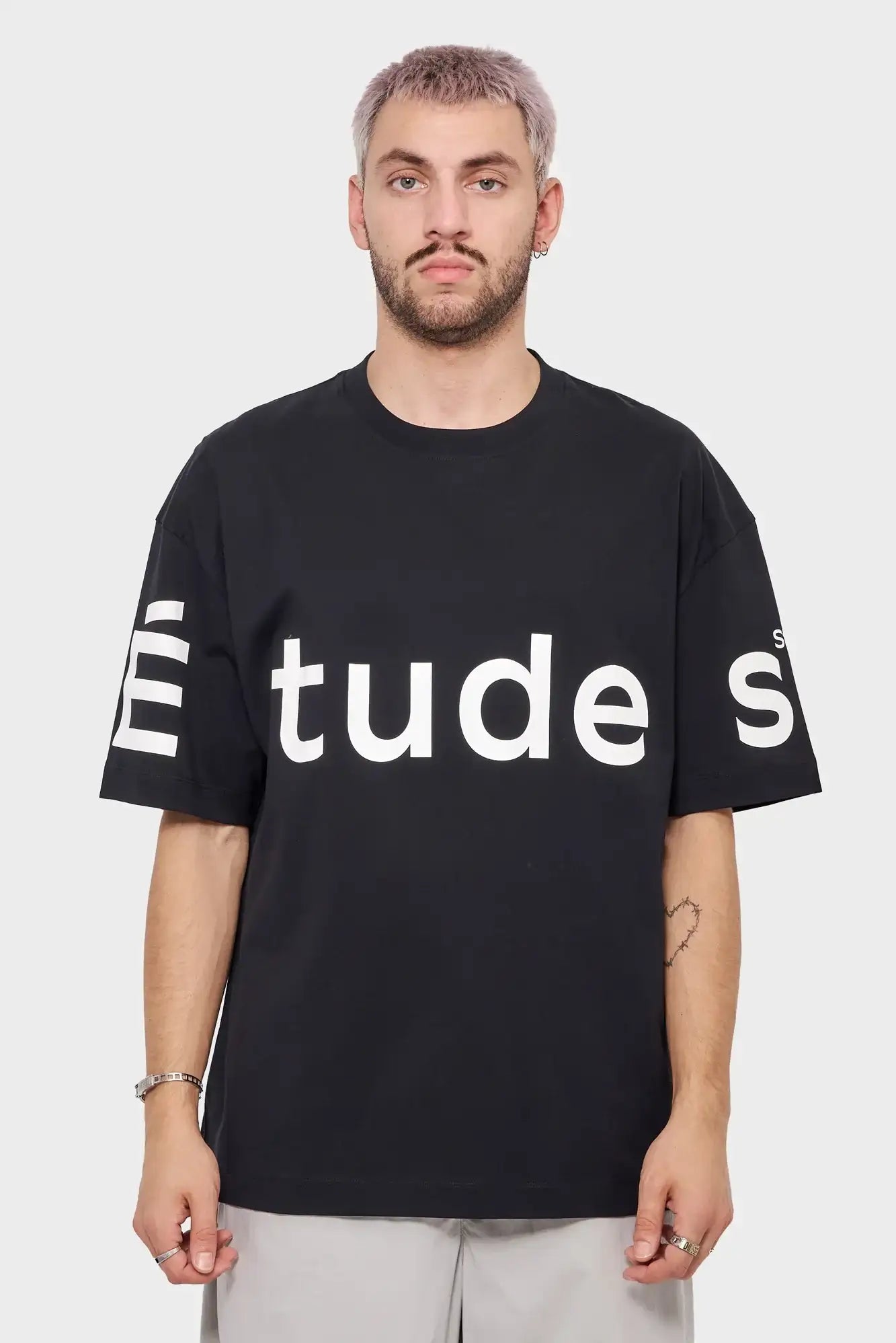 Mężczyzna w czarnej koszulce z dużym białym napisem Études, styl streetwear, tło jasne.