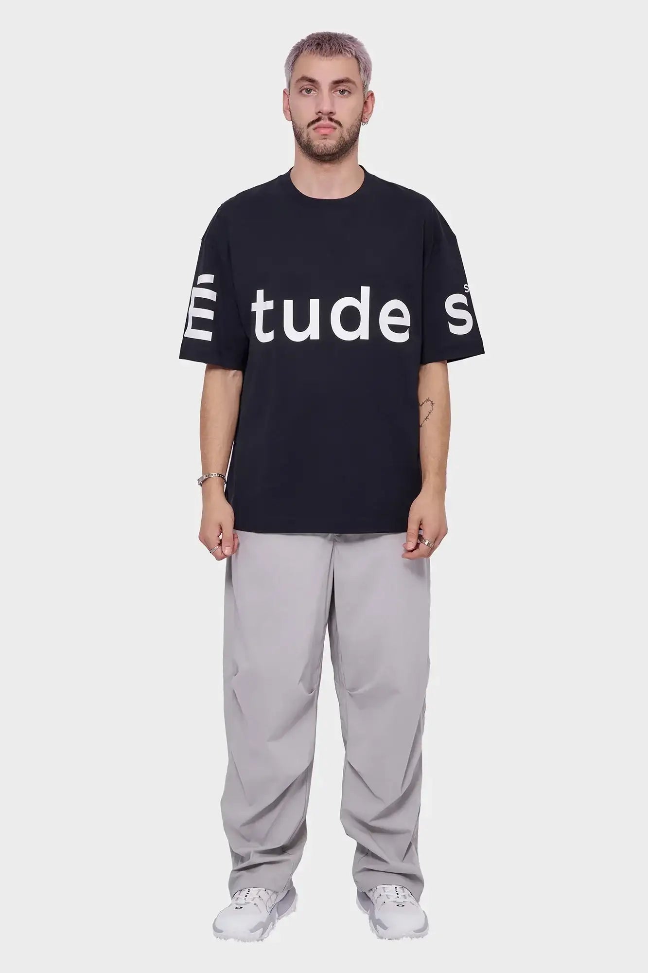 Mężczyzna w czarnym t-shircie z białym napisem, szare spodnie, białe sneakersy, styl streetwear