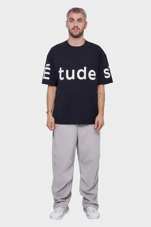 Mężczyzna w czarnym t-shircie z białym napisem, szare spodnie, białe sneakersy, styl streetwear