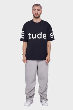 Mężczyzna w czarnym t-shircie z białym napisem, szare spodnie, białe sneakersy, styl streetwear