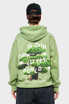 Zielona bluza z kapturem, nadruk drzewo bonsai i napis IN OUR OWN LITTLE WORLD, moda streetwear.