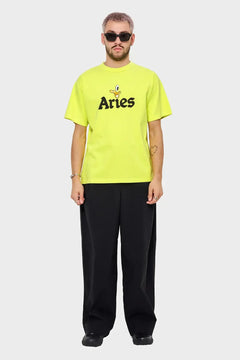 Mężczyzna w neonowej koszulce Aries z nadrukiem, czarne spodnie, nowoczesna moda streetwear