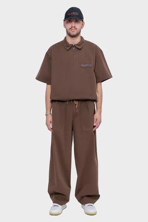 Mężczyzna w brązowym zestawie oversize, spodnie z szerokimi nogawkami, jasne sneakersy, czapka z daszkiem