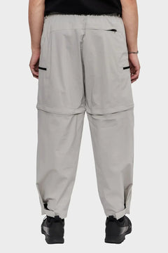 Jasnoszare spodnie typu cargo z kieszeniami, prezentowane od tyłu, styl streetwear.