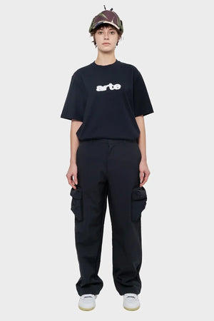 Osoba w czarnym t-shircie z nadrukiem arte, bojówkach i czapce z daszkiem, styl streetwear