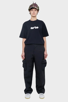 Osoba w czarnym t-shircie z nadrukiem arte, bojówkach i czapce z daszkiem, styl streetwear