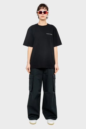 Osoba w okularach przeciwsłonecznych, czarnym t-shircie z napisem, szerokich bojówkach i białych sneakersach, moda streetwear.