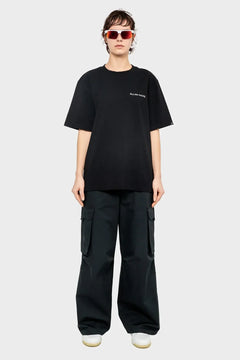 Osoba w okularach przeciwsłonecznych, czarnym t-shircie z napisem, szerokich bojówkach i białych sneakersach, moda streetwear.