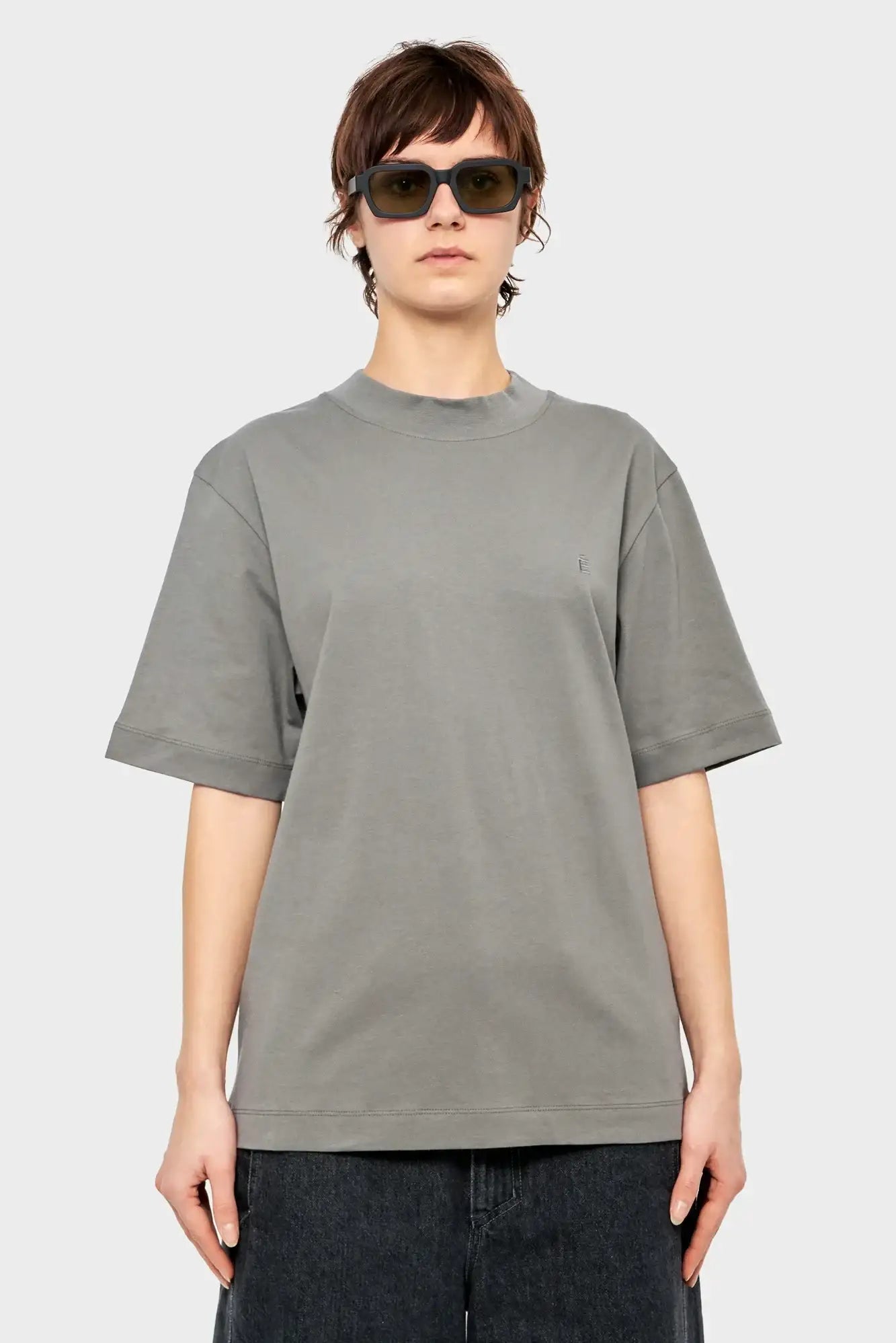 Osoba w szarej oversize koszulce, czarnych okularach przeciwsłonecznych, styl streetwear