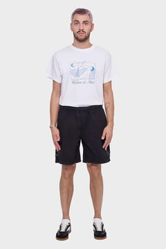 Mężczyzna w białej koszulce z nadrukiem Welcome to Paris, czarnych szortach i sneakersach