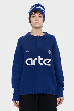 Osoba w granatowym swetrze z nadrukiem arte i granatowej czapce, modna odzież streetwear.