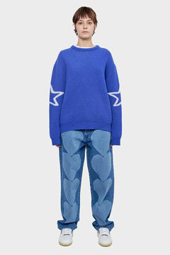 Modelka w niebieskim swetrze z białymi gwiazdami na rękawach i jeansach z wzorem serc, styl streetwear