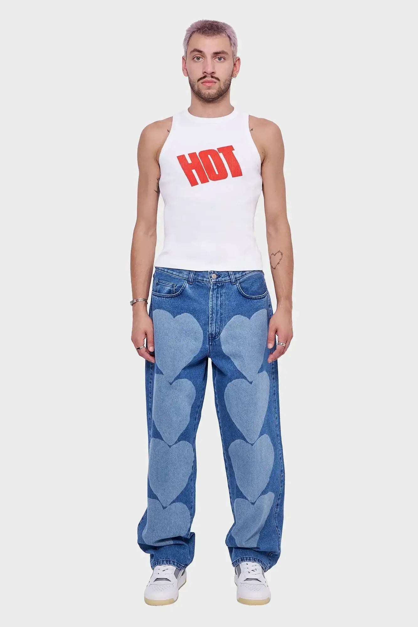 Mężczyzna w białym topie z napisem HOT i niebieskich jeansach z nadrukiem serc, styl streetwear