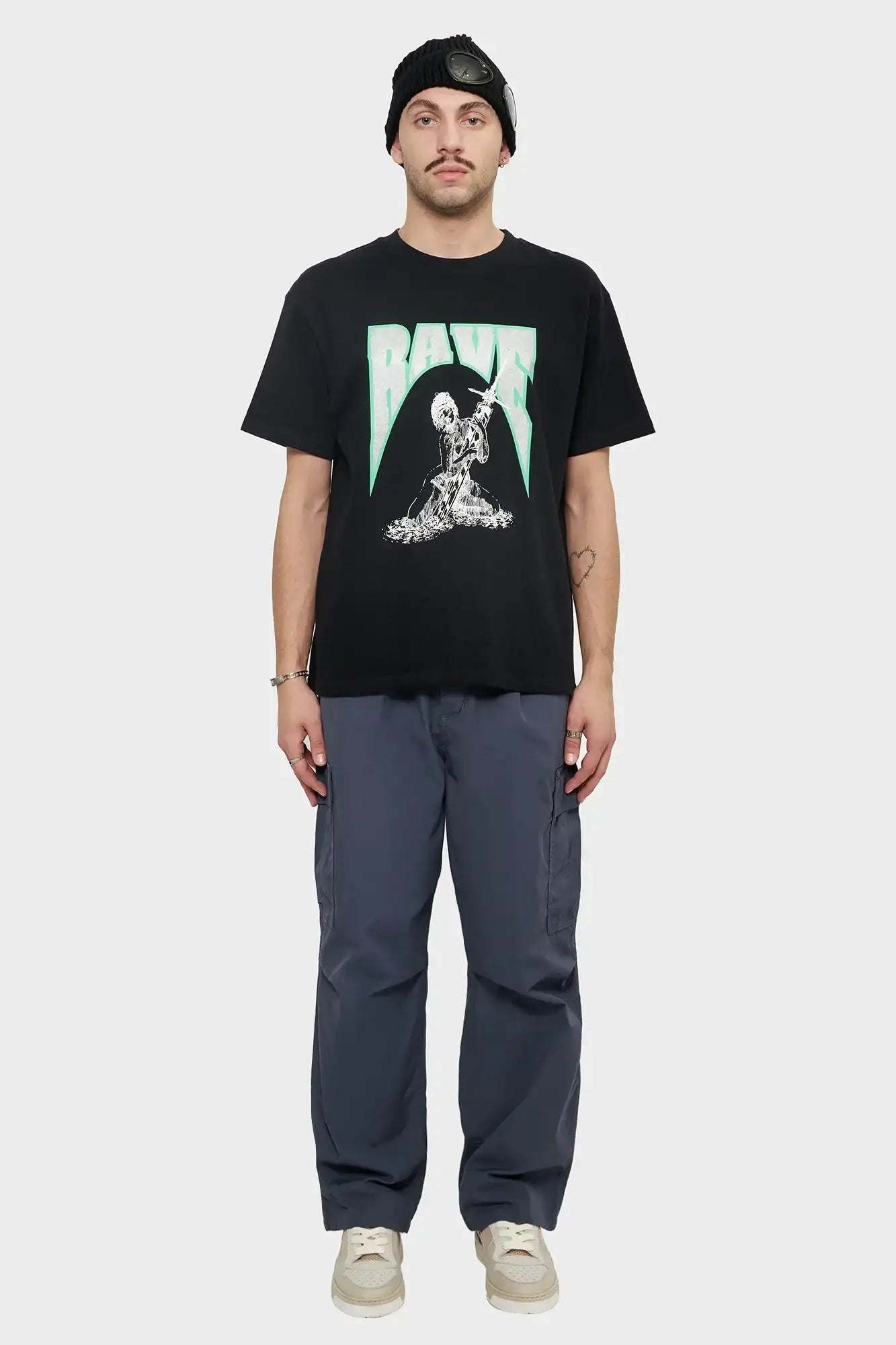 Mężczyzna w czarnym t-shircie z nadrukiem RAVE, szarych spodniach cargo i czapce z okularami