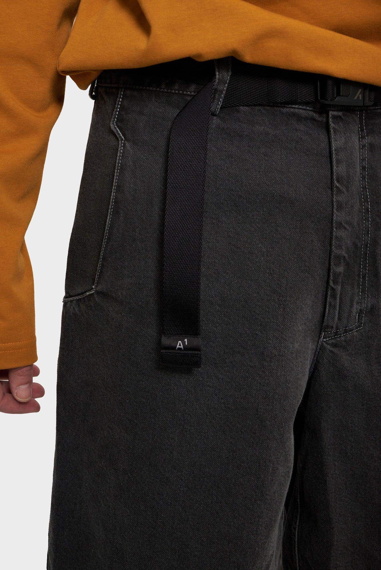 Czarne jeansy z paskiem, detal przy kieszeni, pomarańczowa bluza, moda streetwear