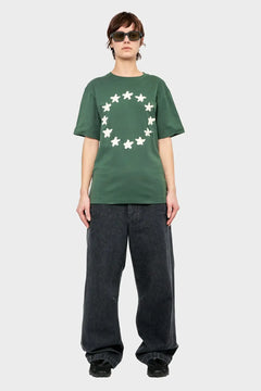 Osoba w zielonej koszulce z nadrukiem białych gwiazd, szerokie czarne spodnie, styl streetwear