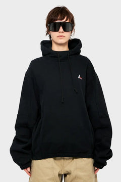 Osoba w czarnej bluzie z kapturem, beżowych spodniach i dużych okularach przeciwsłonecznych, styl streetwear.