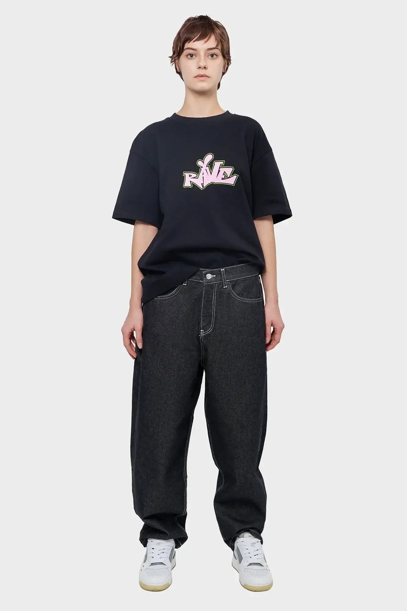 Osoba w czarnej koszulce z napisem RAVE, szerokie jeansy, białe sneakersy, styl streetwear