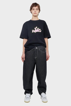 Osoba w czarnej koszulce z napisem RAVE, szerokie jeansy, białe sneakersy, styl streetwear