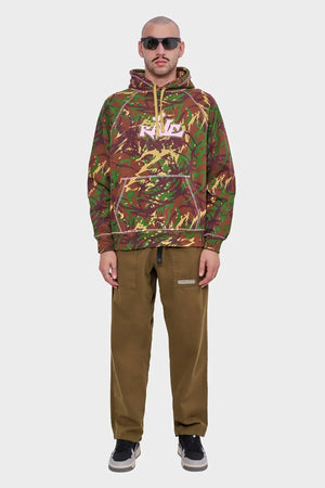 Mężczyzna w bluzie z kapturem w militarny wzór, brązowe spodnie, sneakersy, okulary przeciwsłoneczne