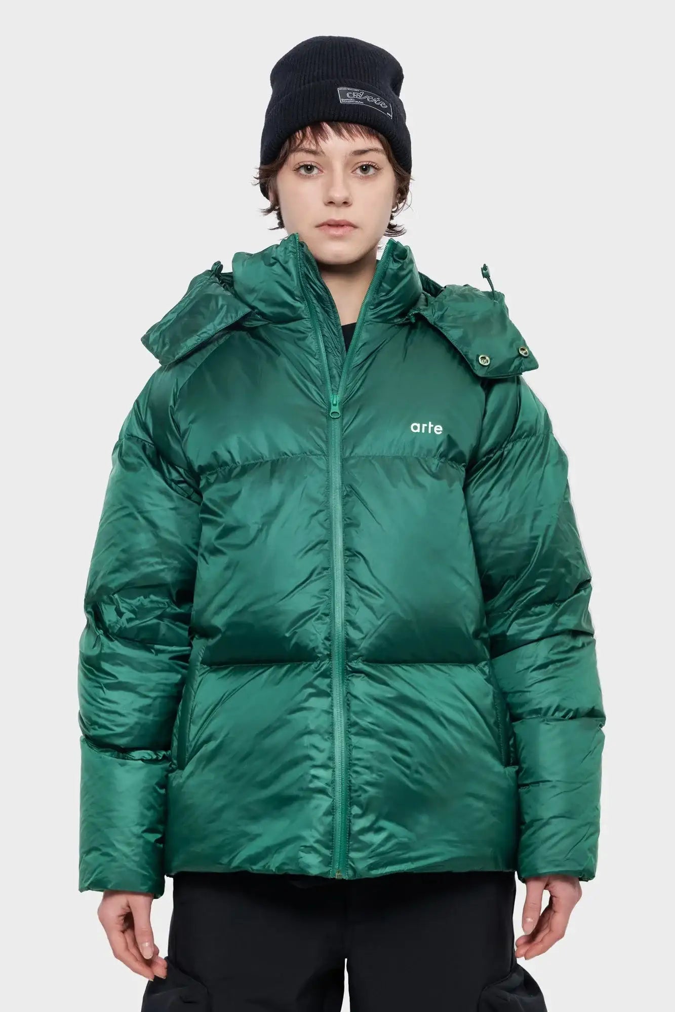 Osoba w zielonej, pikowanej kurtce zimowej z napisem 'arte', czarna czapka, styl streetwear